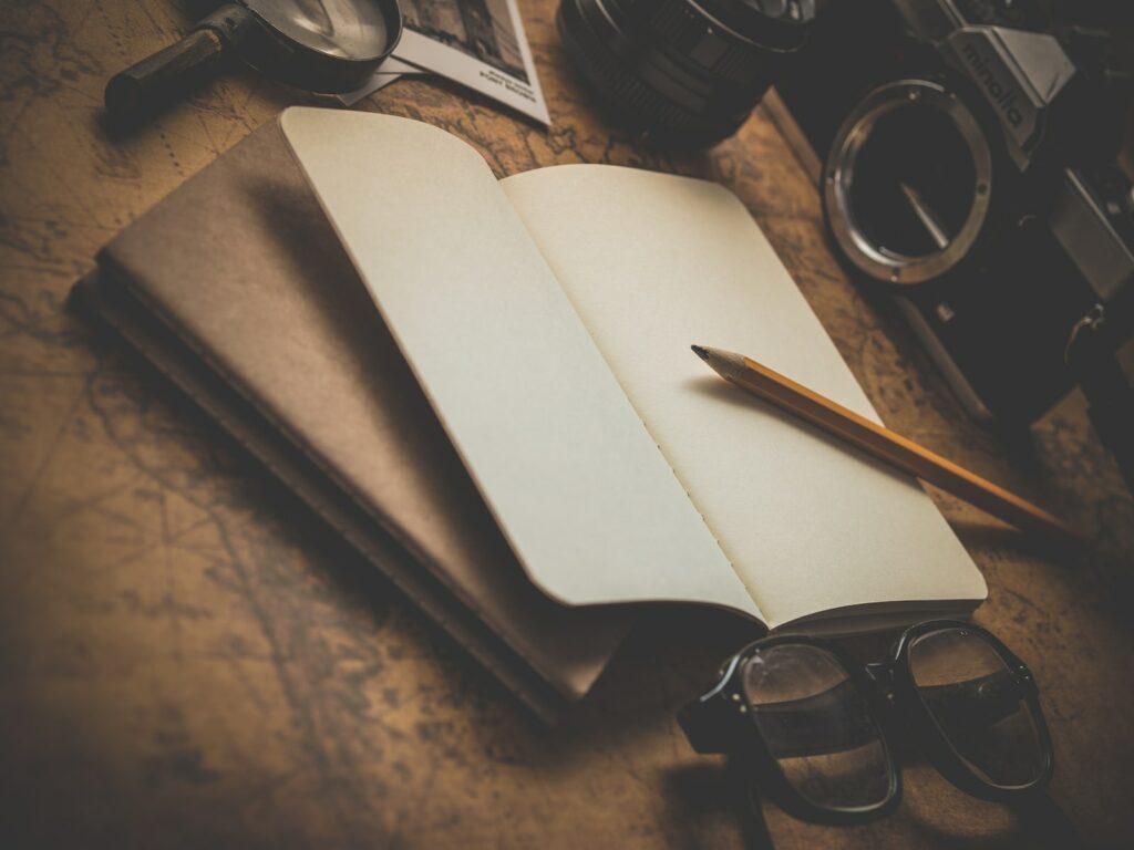 brown pencil on white book beside black eyeglasses